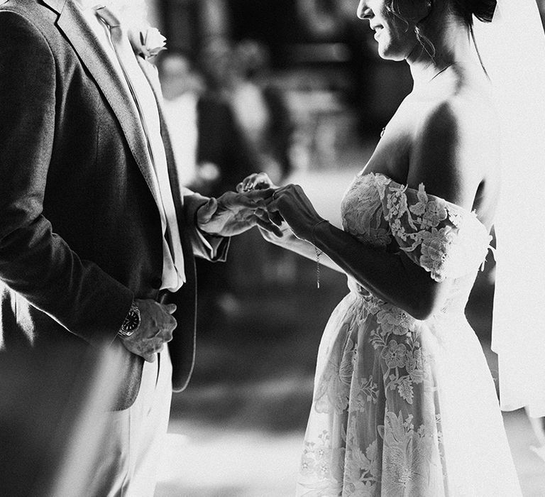 Bride in lace off the shoulder wedding dress puts ring on the groom's finger for civil ceremony at Tythe Barn 