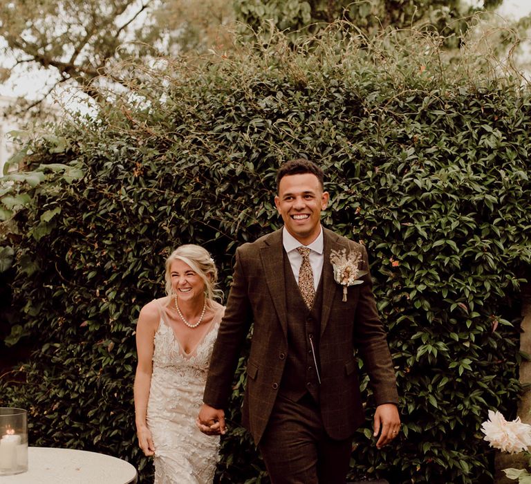 Groom in brown checkered suit and bride in Made With Love Bridal gown enter their reception together