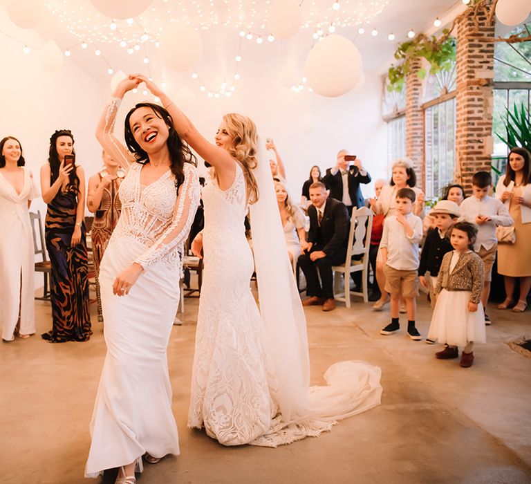 Bride dance together under white balloon and fairy light decoration with guests and children watching on