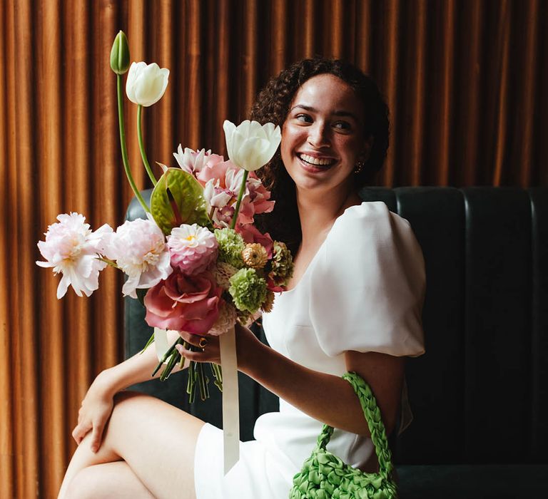 Bride in a short wedding dress holding a satin crochet bag and pink and white wedding bouquet 