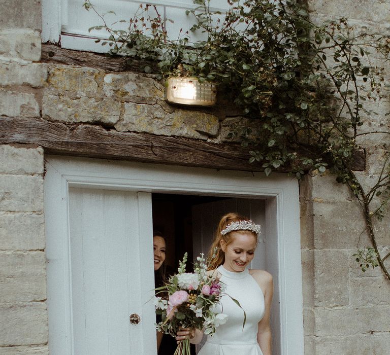 Bride in halter neck wedding dress with pleated skirt and pearl embellished wedding shoes carrying white and pink bouquet 