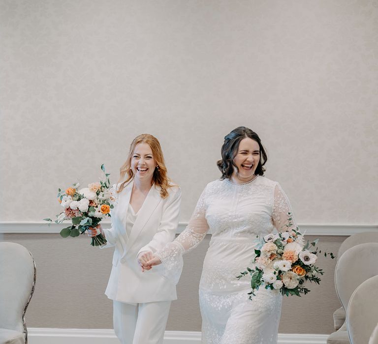 Brides hold hands as they walk with one another on their wedding day