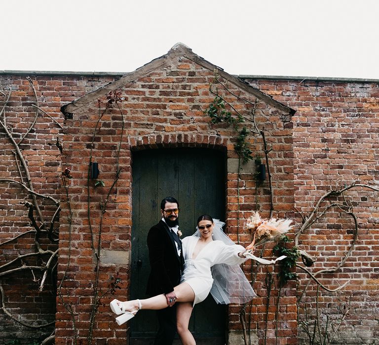 Stylish bride and groom in a tuxedo and white block heels and a short wedding dress at Garthmyl Hall 