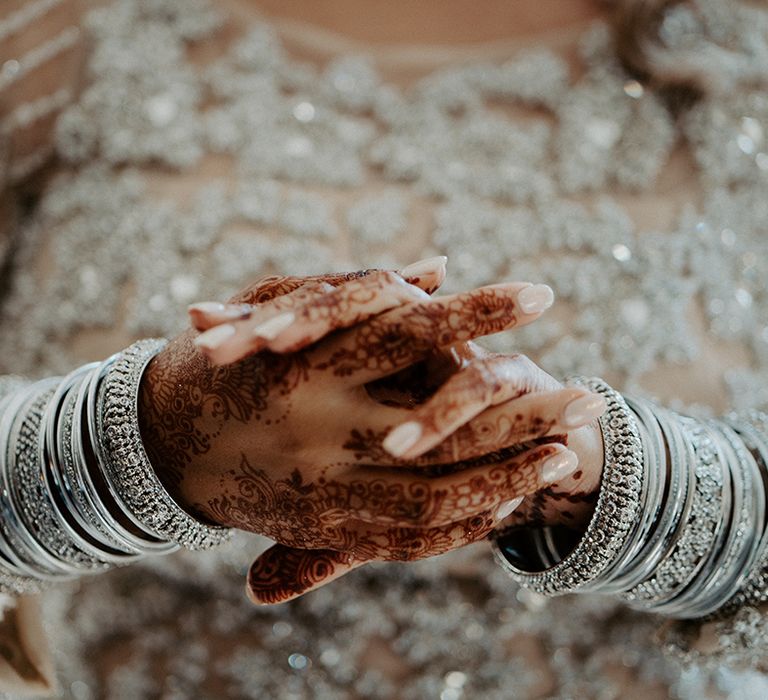 Brides hands featuring nude nail varnish, silver bangles and henna 