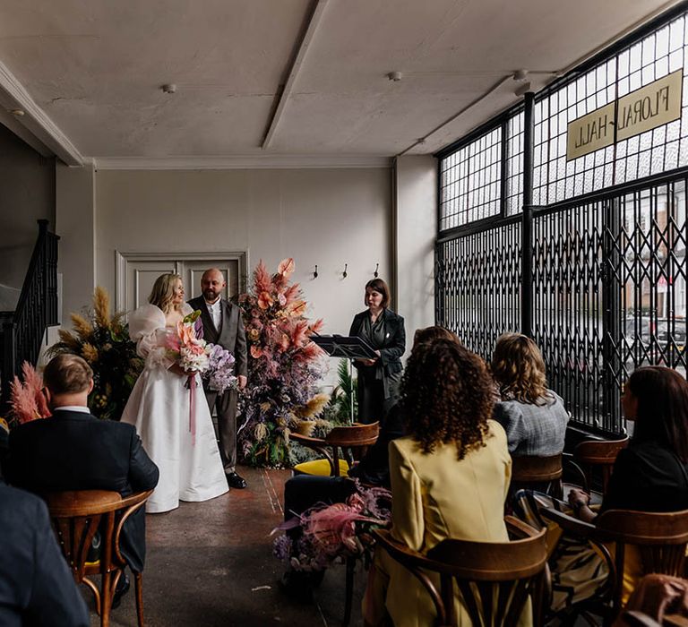 Floral Hall humanist wedding ceremony with column flowers at the altar, bride in a JESUS PEIRO wedding dress and groom a double breasted jacket 