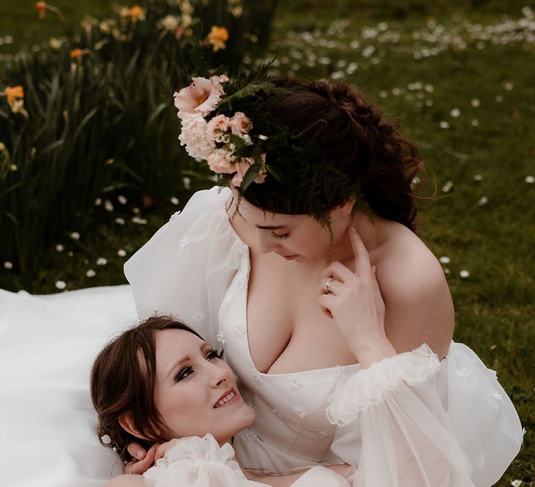 Bride in an ethereal wedding dress with long sheer sleeves laying on her brides lap in a strapless wedding dress with V front and puff sleeves