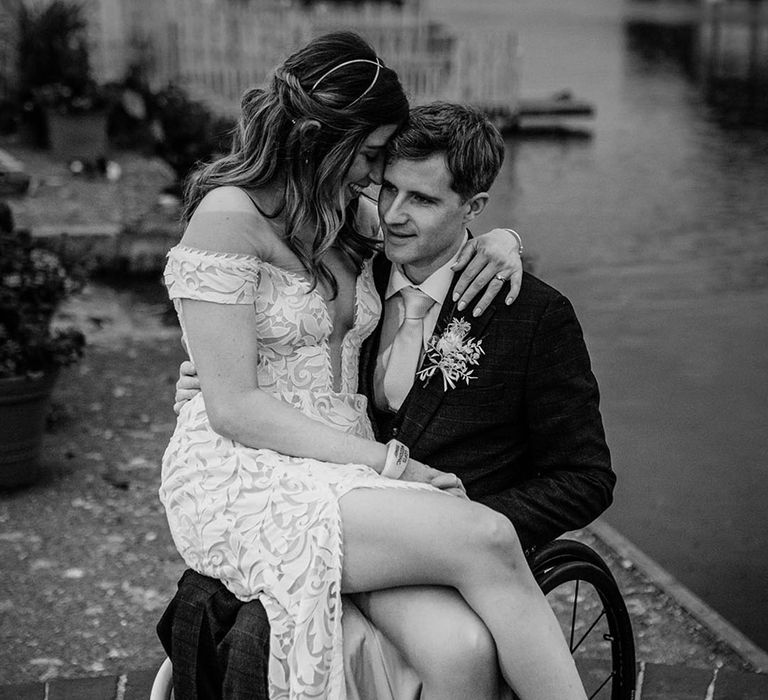 Bride sits on the groom's lap and rests her forehead against the groom's head 