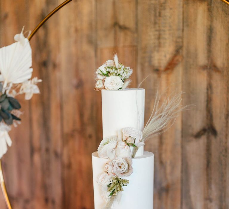 Tall three tier white wedding cake with pink rose flower decoration and dried grass