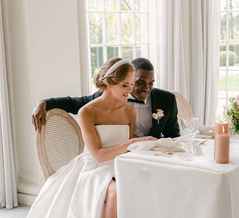 Stylish bride and groom sit together as they look through their wedding menu together 