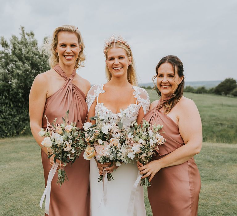 Bride in flower embellished crown, cape and handmade wedding dress with bridesmaids in dusty rose satin dresses