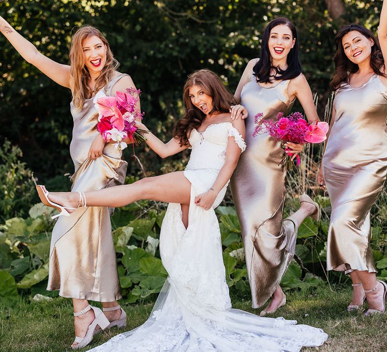 Bride stands with her bridesmaids who wear champagne bridesmaid dresses whilst holding bright floral bouquets 