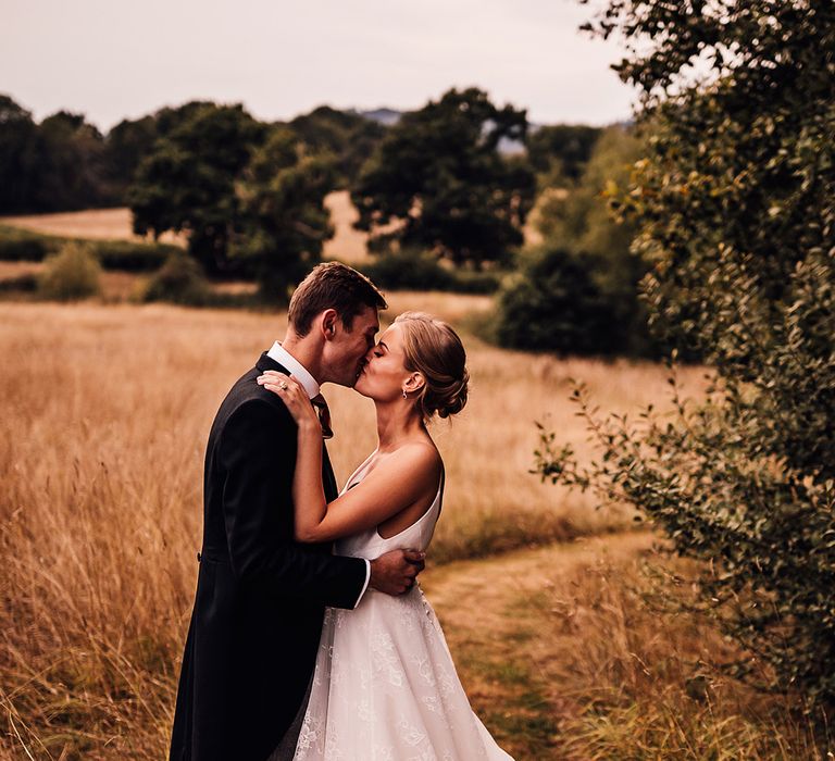 Bride and groom share a kiss as they stand in a field 