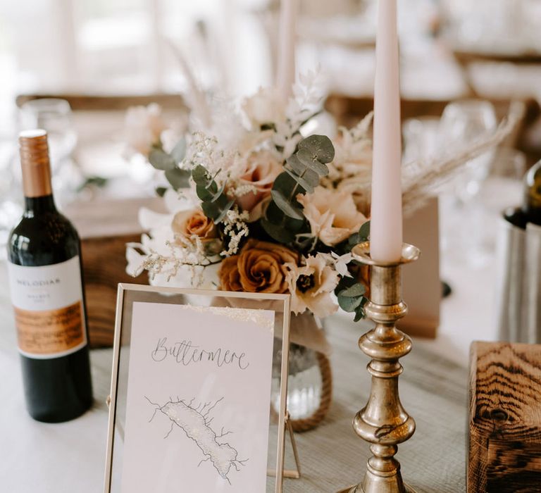 Hand drawn wedding table names with white taper candles with small orange and white flower arrangements 