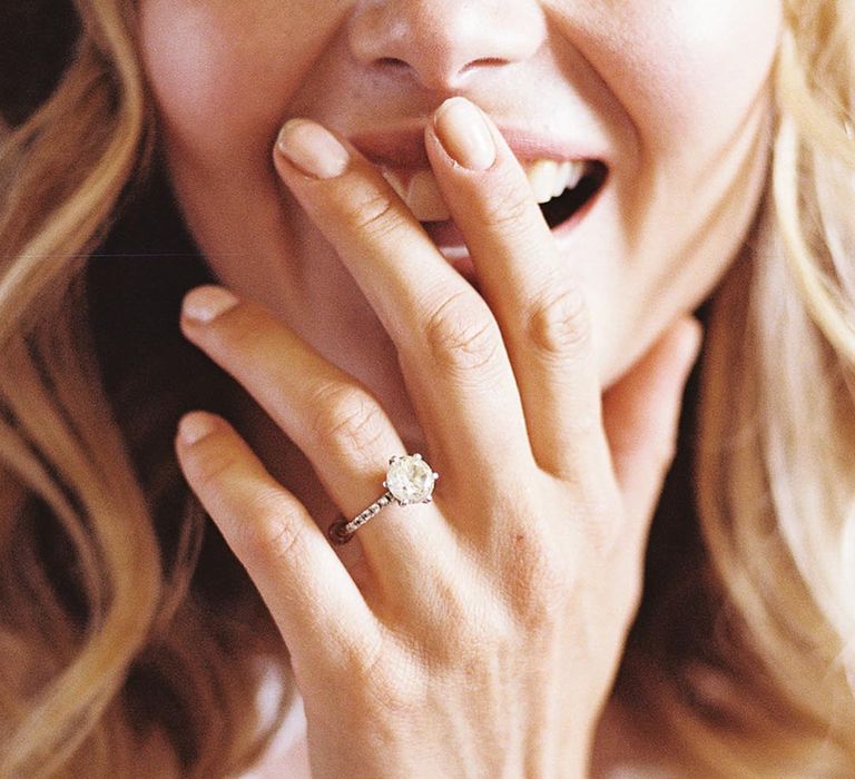 Bride in a lace long sleeve wedding dress shows off her round engagement ring 