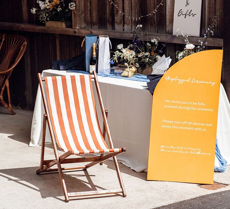 Table for the wedding cards and gifts with a yellow wedding sign for the unplugged wedding ceremony and a deck chair 