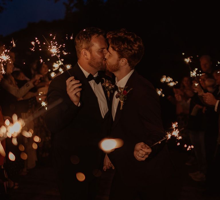 Grooms share a kiss as they have a sparkler send off after their autumn wedding 