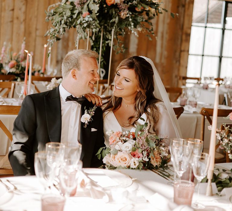 Bride & groom sit in reception surrounded by floral installations with pops of orange 