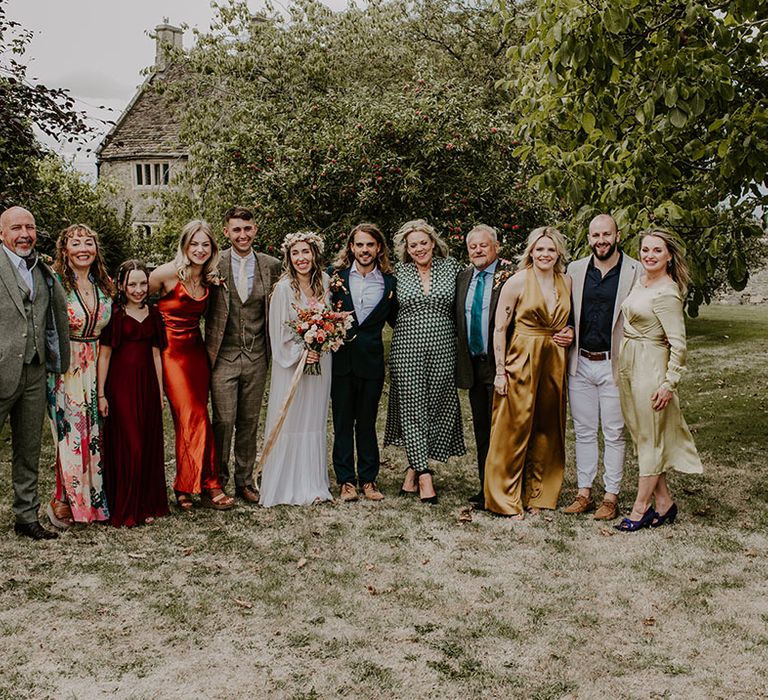 Bride & groom stand with wedding party outdoors with bridesmaids in Autumnal coloured dresses 