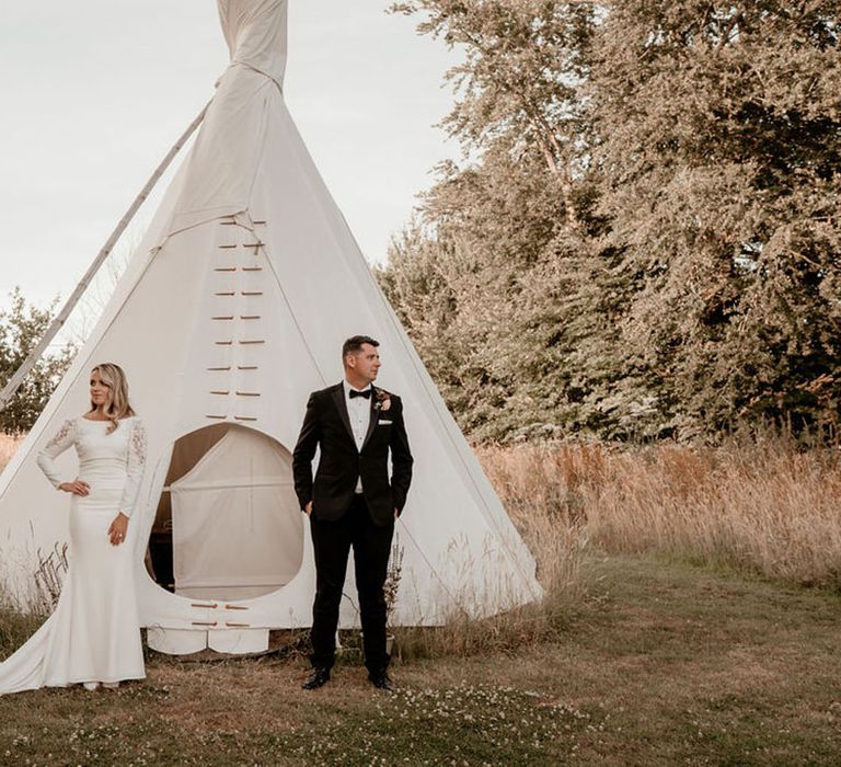 Bride and groom standing in front of mini tipi 