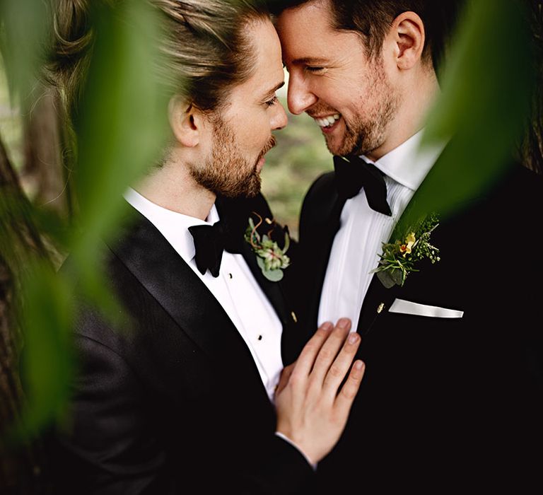 Grooms in black-tie embrace lovingly outdoors after wedding ceremony