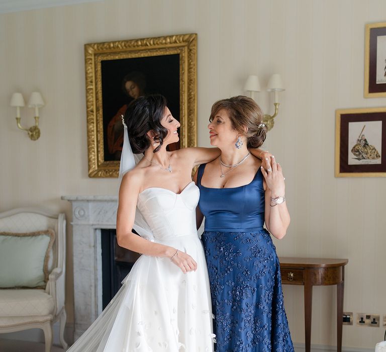 Bride stands with her mother who wears royal blue silk fitted dress with embellished skirt 