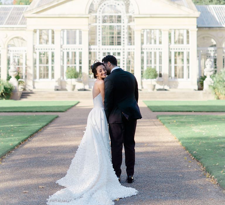 Bride & groom stand in front of Syon Park Conservatory during couples portraits