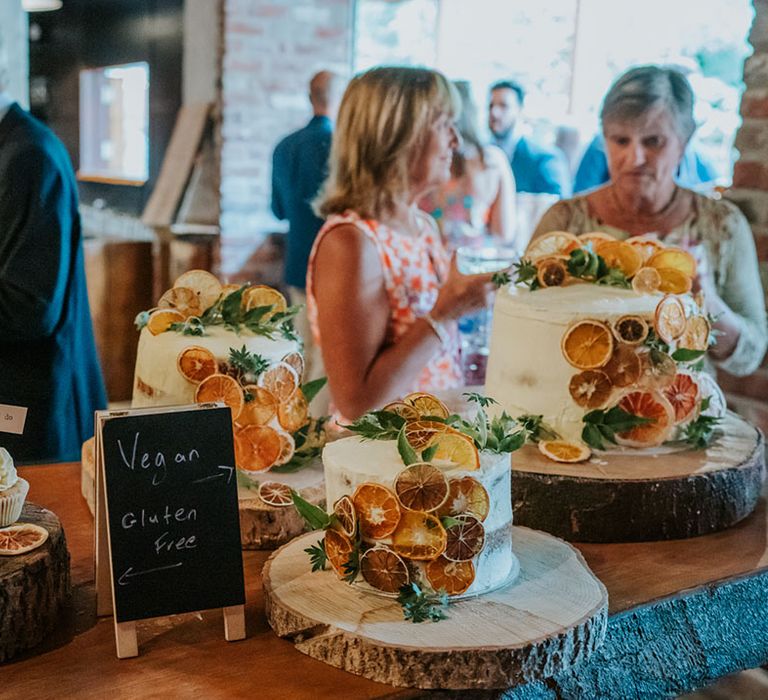 The dessert table with gluten free vanilla cupcakes and lots of frosted vegan wedding cakes decorated with dried orange slices 