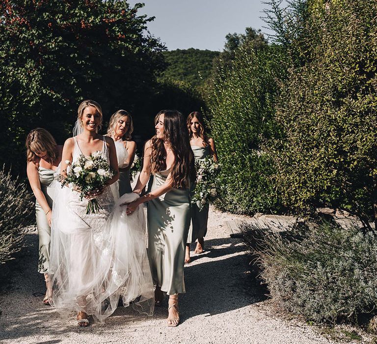 Bride carries white floral bouquet alongside her bridesmaids in pale green satin bridesmaid dresses 