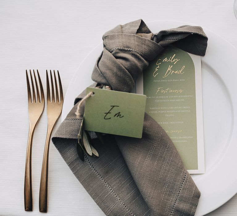 Green name cards and menu beside fabric napkin and gold cutlery 