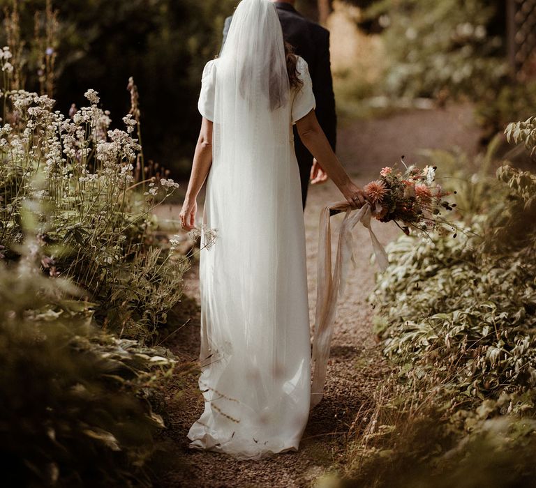 Bride in button back wedding dress with veil walking with the groom holding a rustic wedding flower bouquet 