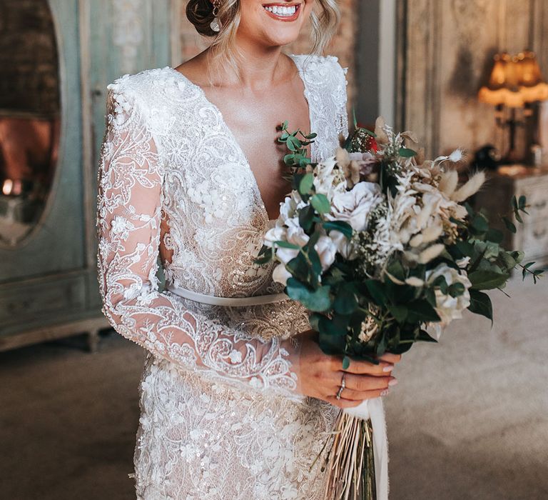 Bride wearing a sparkly intricate low cut wedding dress with shoulder pads holing a dried flower wedding bouquet with pearl earrings 