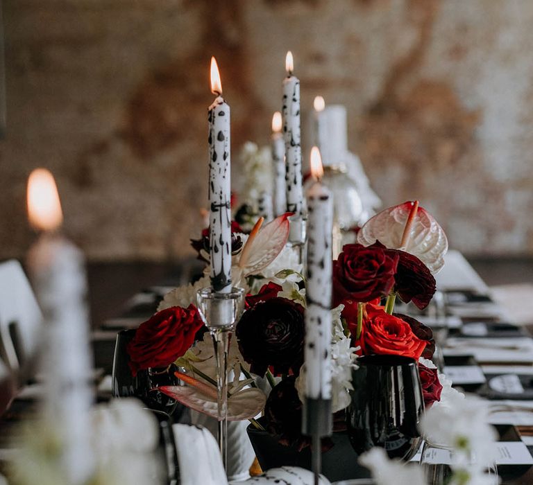 Black and white tapered candles in the style of Dalmatian print, red roses and black sculptures at Woolwich Works London wedding venue 