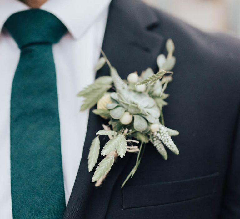 Dark wedding suit worn by groom with green tie and all foliage buttonhole groom accessory 