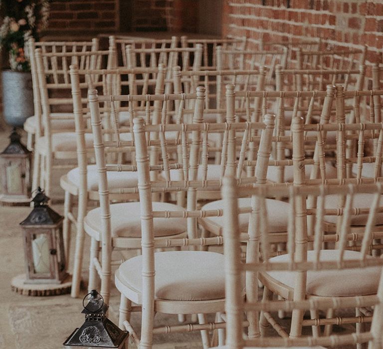 White wooden wedding chairs with small metal lanterns resting on tree trunk slices for the aisle decorations