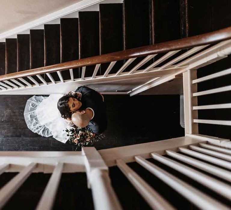 Bride in square neck puff sleeve wedding dress with embroidered veil embracing groom by the staircase 