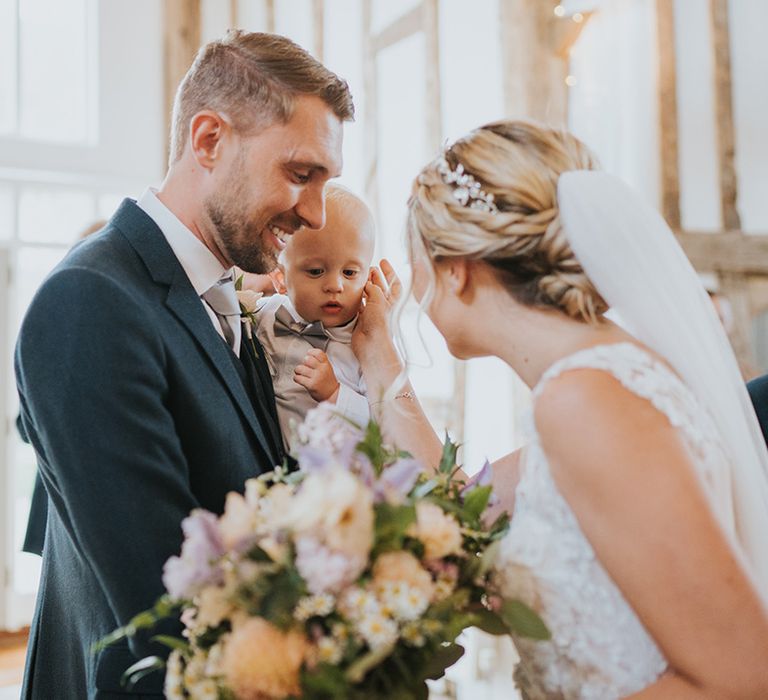 The groom holds his son as they stand at the altar for the wedding ceremony with the bride showing their son some love 