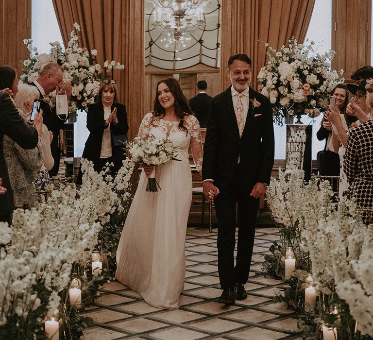 Claridge's wedding with the bride in a maternity wedding dress with lace detail and groom in suit walking back down the aisle as a married couple