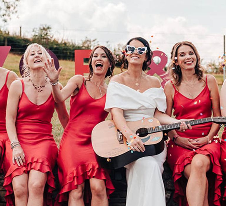 Bridesmaids in ruffle orange midi dresses for fun festival wedding with the bride wearing white retro sunglasses 