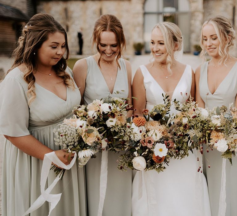 Bridesmaids in sage green satin bridesmaid dresses holding neutral wedding bouquets with the bride in a Maggie Sottero wedding dress 