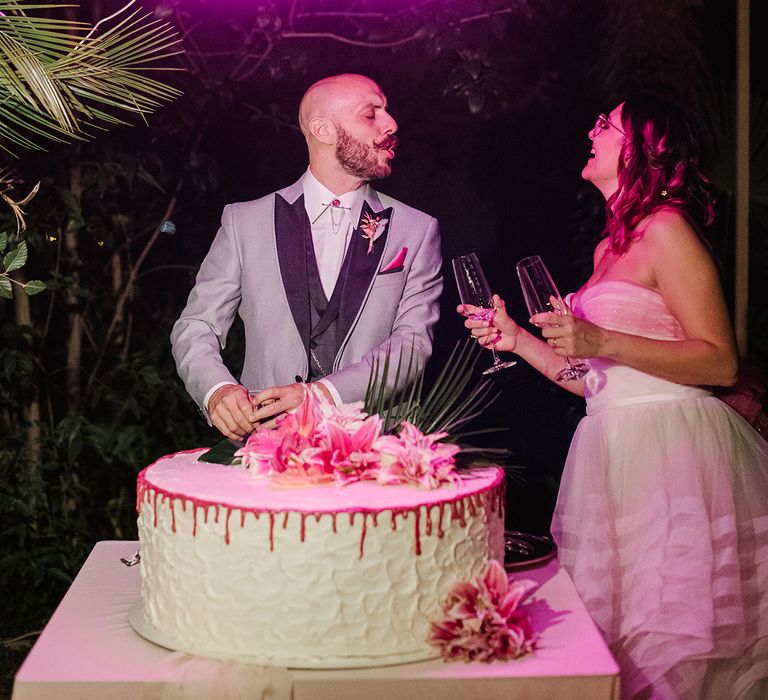 bride and groom cutting their giant single tier drip wedding cake under a neon pink wedding sign