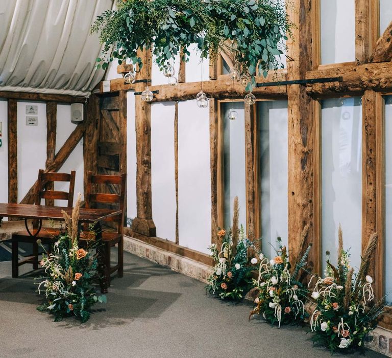 South Farm wedding venue ceremony room with exposed wooden beams, suspended foliage decor and pampas grass, eucalyptus, blush garden roses, dried flowers and foliage arrangements