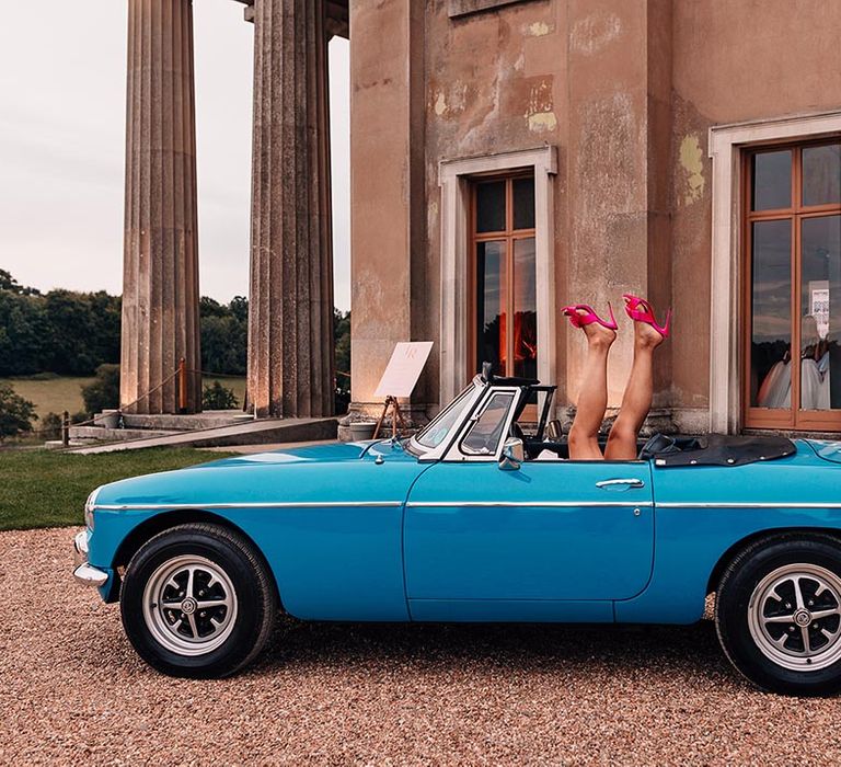 Vintage blue wedding car with the bride lifting her legs in the air to show off her hot pink Louboutin shoes 