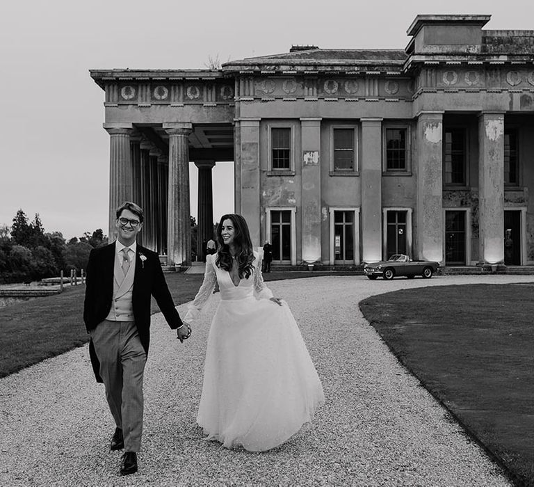 The Grange country house wedding venue in Hampshire with the bride and groom walking hand in hand on the driveway 