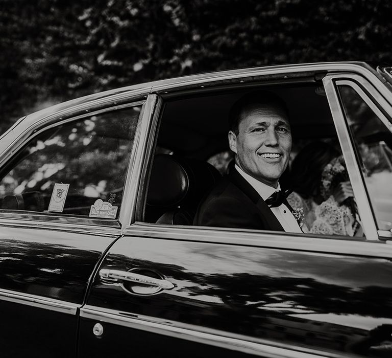 black and white photo of the groom in a bow tie sitting in a vintage wedding car