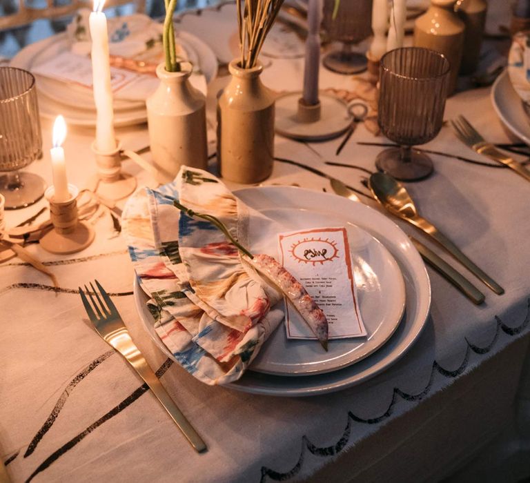 Eclectic abstract wedding tablescape at Margate Caves - neutral toned under table cloth, abstract design wedding tablecloth on top, twisted tapered candles in ceramic candlestick holders, gold cutlery, abstract wedding stationery, and dried flower centrepieces