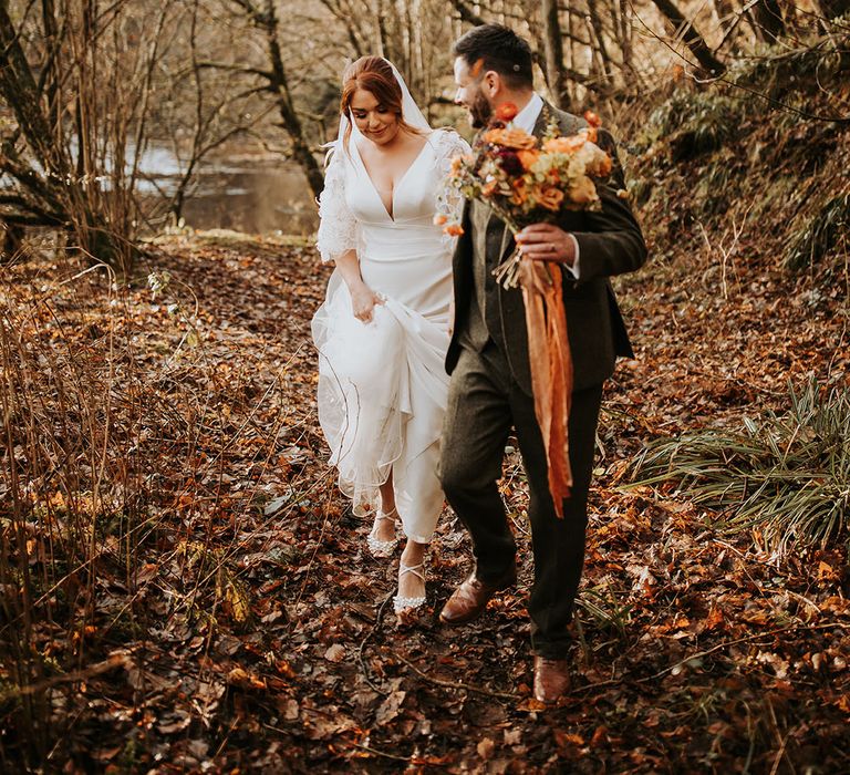 Bride wearing pearl heel wedding shoes and Suzanne Neville wedding dress with groom in three piece suit 