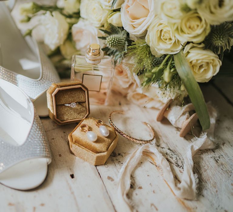 Bridal accessories with a white rose bouquet, Chanel perfume and sparkly wedding shoes with a mustard yellow box with pearl earrings 