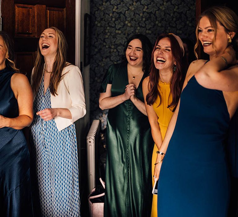 Bridesmaids in mismatched green, blue, and yellow bridesmaid dresses getting their first look at the bride 