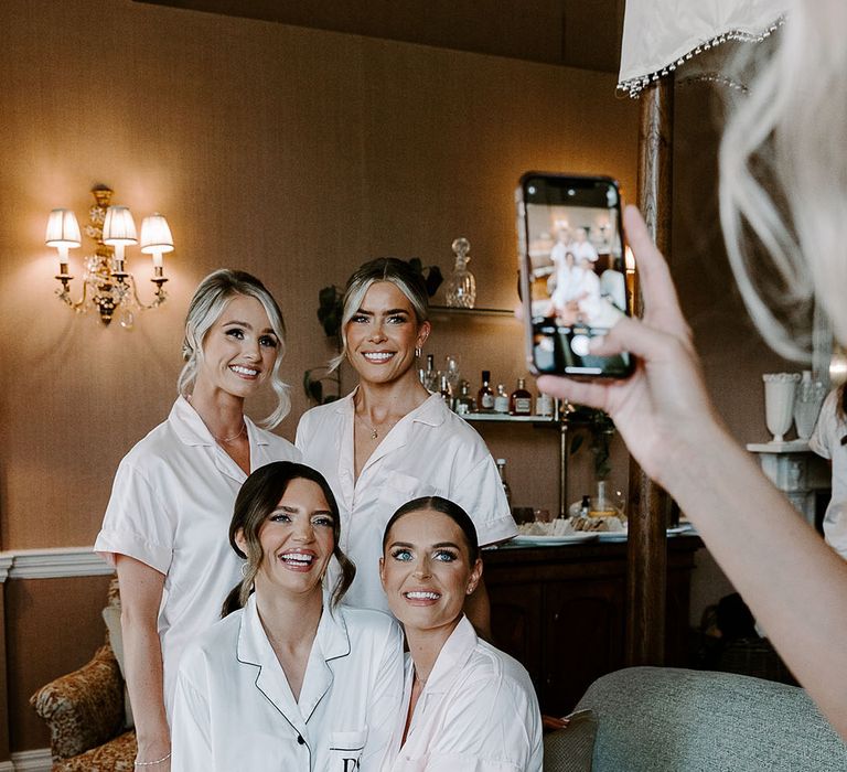 Bride and bridesmaids in white satin pyjamas getting ready in the morning together 