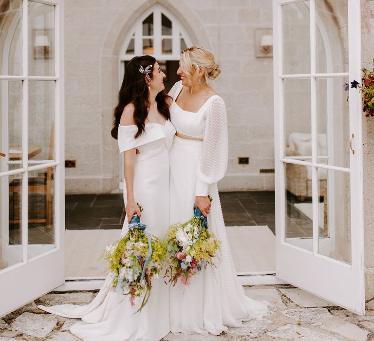 Romantic whimsical wedding with the two brides posing together carrying their wildlflower wedding bouquets for whimsical wedding 